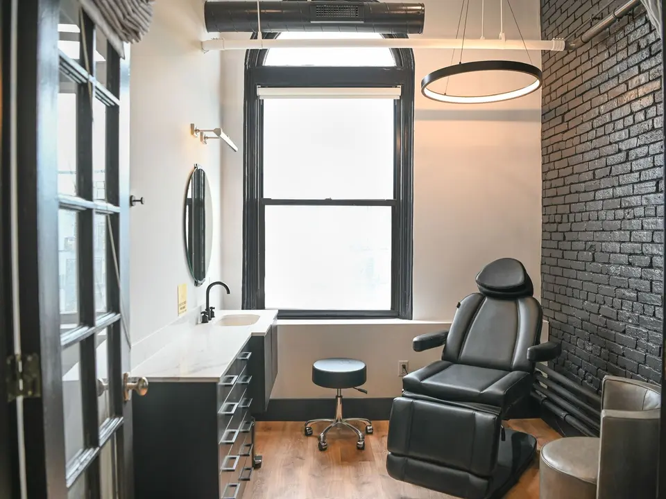 Empty treatment room at Boston Beautox with procedure chair and black brick accent wall
