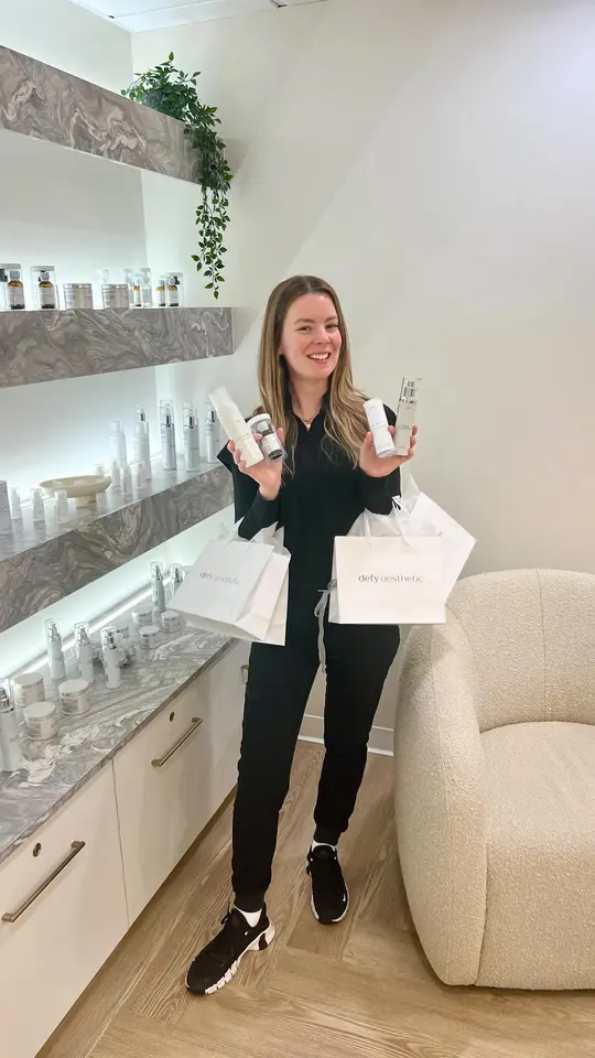 Defy Aesthetic staff member with retail skincare shelving in the studio